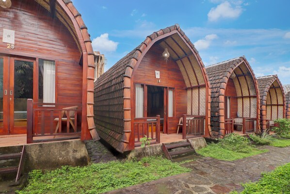 A row of wooden cabins with arched roofs, wooden railings, and a stone pathway leading to the entrance. - Hotel O near Mookiland Park Bali formerl (Keroboken Kelod)