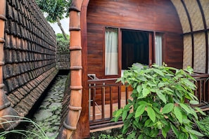 A wooden building with a balcony, a stone wall, and a green plant. - Hotel O near Mookiland Park Bali formerl (Kerobokan)