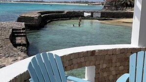 A balcony with two blue Adirondack chairs, a stone wall, and a view of the ocean and a lighthouse. - Terrace with sea views! #Amazing sea views! (Santa Maria)