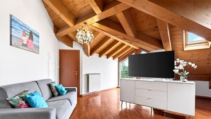 Un salón moderno con techo de madera, un sofá gris con cojines azules, un mueble de entretenimiento blanco y un televisor grande.
