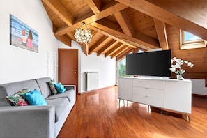 Un salon moderne avec un plafond en bois, un canapé gris agrémenté de coussins bleus, un meuble de télévision blanc et un grand écran.