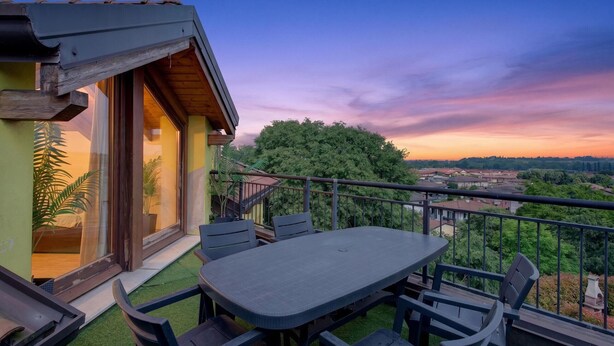 Un balcón con mesa y sillas, con vistas a un paisaje de árboles y edificios.
