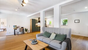 Una sala de estar moderna con un sofá gris, una mesa de centro de madera y una cocina al fondo.