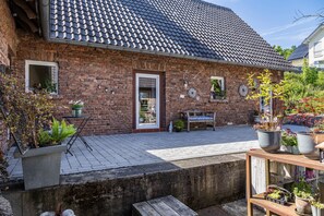 A brick building with a tiled roof, a wooden bench, and potted plants.