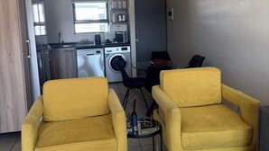 A modern living space with a kitchen, two yellow armchairs, a small dining table, and a washing machine. - 2 minutes to the mall, restaurants gym, shops all amenities 2 minutes away. (Sandton)