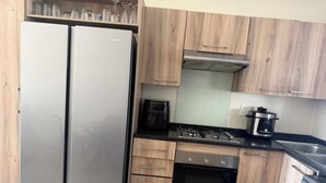 A kitchen with a stainless steel refrigerator, a gas stove, an oven, wooden cabinets, and a coffee maker. - 2 minutes to the mall, restaurants gym, shops all amenities 2 minutes away. (Sandton)