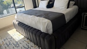 A modern bedroom with a large bed, a view through a window, and a patterned rug. - 2 minutes to the mall, restaurants gym, shops all amenities 2 minutes away. (Sandton)