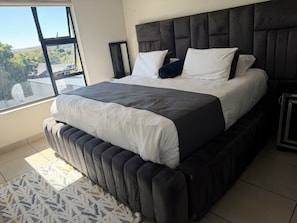 Ein modernes Schlafzimmer mit einem großen Bett, einem Ausblick durch ein Fenster und einem gemusterten Teppich.