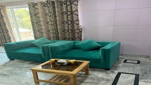 A teal sofa, a wooden coffee table, and patterned curtains in a room with a tiled floor. - Hotel Hayatt Sukkur (Sukkur)