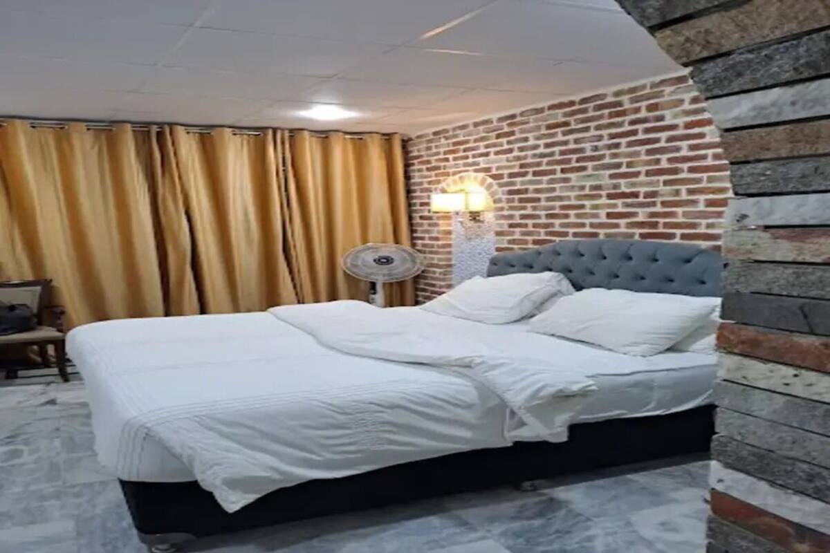 A hotel room with a bed, curtains, a lamp, and a brick wall.