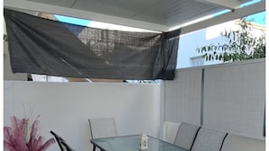 A covered patio area with a glass table and chairs, a potted plant, and a view of the outside. - Central Paroikia Apartment - 10min walk to Port and Beach! (Paros)