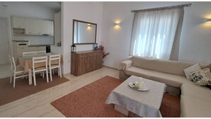 A living room with a sofa, a dining table with chairs, a kitchen area, and a large mirror. - Central Paroikia Apartment - 10min walk to Port and Beach! (Paros)