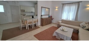 A living room with a sofa, a dining table with chairs, a kitchen area, and a large mirror. - Central Paroikia Apartment - 10min walk to Port and Beach! (Paros)