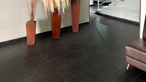 Eine Lobby mit einer Treppe, dunklen Fliesenböden und drei großen Kübelpflanzen.