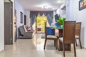 Una sala de estar moderna con sofá, mesa de comedor, sillas y un amplio ventanal con cortinas.