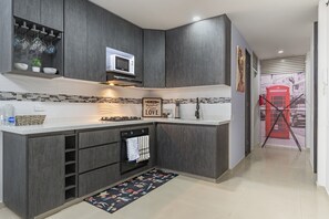 A modern kitchen with dark cabinetry, a microwave, and a red telephone booth decoration. - Modern 2BR with pool in Tequendama Cali. (Cali)