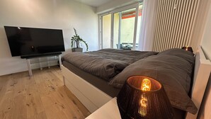 A bedroom with a bed, a TV, a plant, and a window with blinds. - Bella-Lugano vacation apartment (Aldesago)