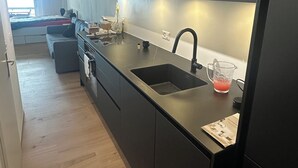 A modern kitchen with a black countertop, stainless steel sink, and a window providing natural light. - Bella-Lugano vacation apartment (Aldesago)