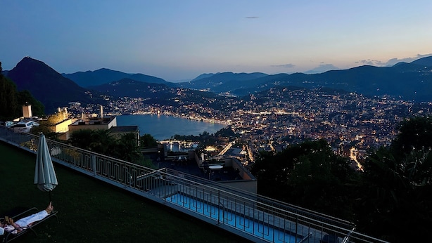 A panoramic view of a city at dusk with a pool area in the foreground. - Bella-Lugano vacation apartment (Aldesago)