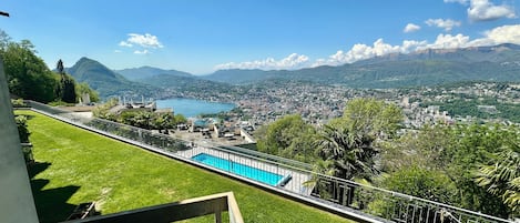 A pool with a view of a lake and mountains, a grassy area, and a railing.