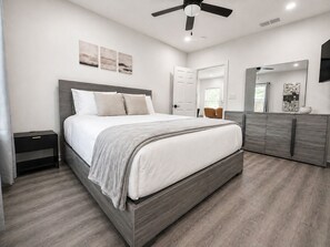 A modern bedroom with a bed, nightstand, dresser, ceiling fan, and artwork on the wall. - Fire Pit Home by Mercedes-Benz Stadium (Atlanta)