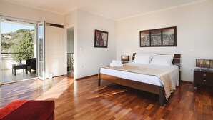 A bedroom with a bed, a nightstand, a TV, and a sliding glass door leading to a balcony. - Villa Amarandes With Private Pool (Rhodes)
