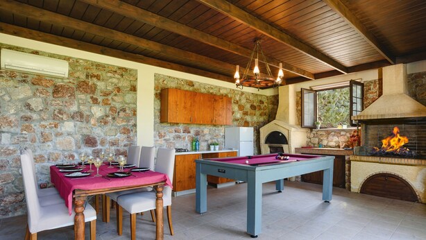 A dining area with a pool table, a kitchen with stone walls, and a fireplace. - Villa Amarandes With Private Pool (Rhodes)