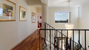 A staircase with ornate black railings, a chandelier, and framed artwork on the walls. - Villa Amarandes With Private Pool (Rhodes)