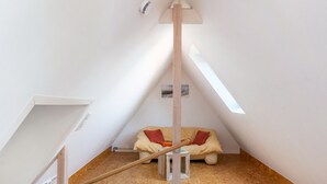 A small, triangular attic room with a slanted ceiling, a wooden beam, a small stool, and a sofa with cushions. - Holiday Apartment 'Glück in Dornum' with Wi-Fi (Dornum)