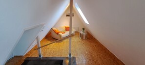 Eine schmale Treppe führt zu einem Schlafzimmer im Podestbereich mit schrägem Dach, einem Sofa, einem kleinen Tisch und einer Pflanze.