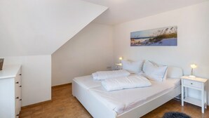 A bedroom with a bed, bedside tables, a painting, and a sloped ceiling. - Holiday Apartment 'Glück in Dornum' with Wi-Fi (Dornum)