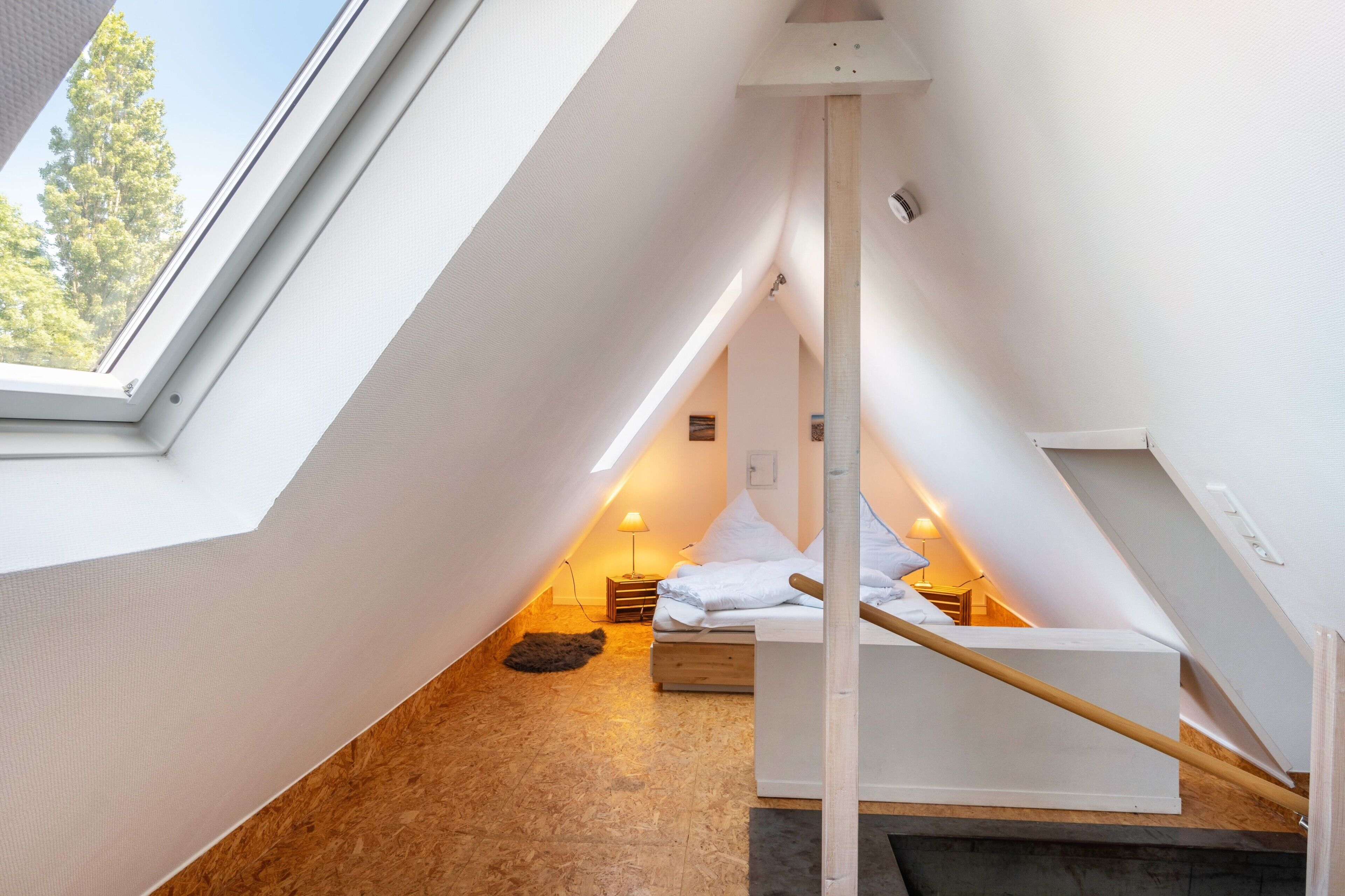 A small, sloped-roofed attic bedroom with a bed, bedside tables, and a skylight.