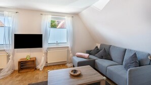 A modern living room with a flat-screen TV, a grey sofa, and a wooden coffee table. - Holiday Apartment 'Glück in Dornum' with Wi-Fi (Dornum)