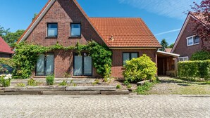 A brick house with a red-tiled roof, a wooden front porch, and a paved driveway. - Holiday Apartment 'Glück in Dornum' with Wi-Fi (Dornum)