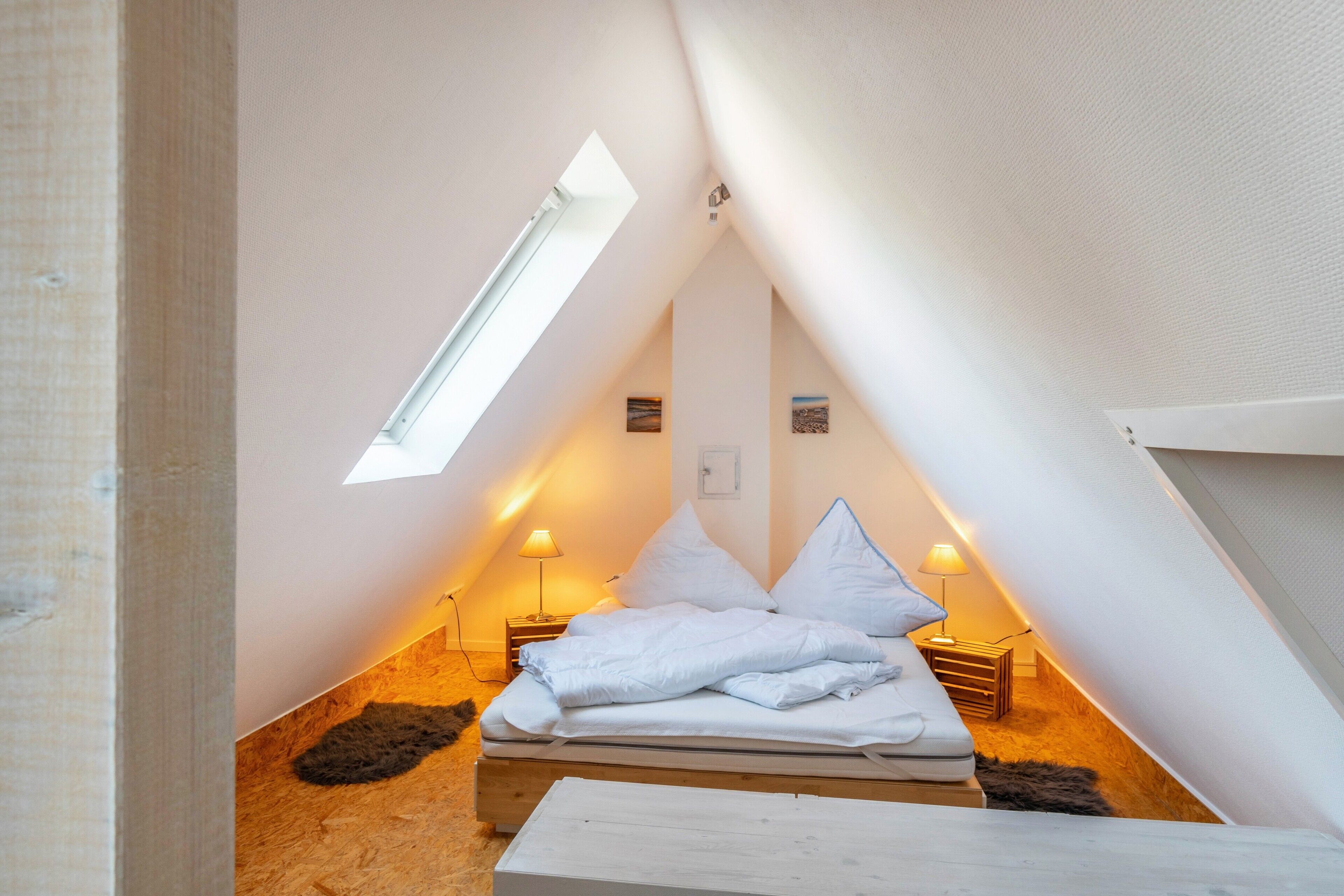 A small, triangular attic bedroom with a bed, two bedside lamps, and a skylight.