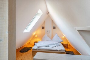 A small, triangular attic bedroom with a bed, two bedside lamps, and a skylight. - Holiday Apartment 'Glück in Dornum' with Wi-Fi (Dornum)