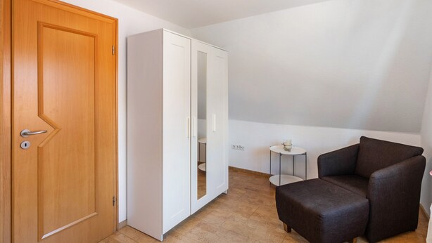 A room with a wooden door, white wardrobe, small round table, and a dark brown chair. - Holiday Apartment 'Glück in Dornum' with Wi-Fi (Dornum)