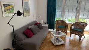 Una habitación amoblada con un sofá, dos sillones de mimbre, una mesita, una lámpara y obras de arte en la pared.