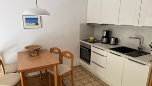 Cocina compacta con armarios blancos, una mesa de comedor de madera y piso con estampado en espiga.
