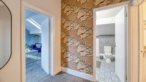 A hallway with a patterned wall, a blue sofa, a coffee table, and a view into a bathroom with a toilet and sink. - Glendale House by Guestz (Lytham-St-Annes)