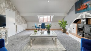 A spacious loft with a high ceiling, a dining area with blue chairs, a fireplace, and a television on the left. - Glendale House by Guestz (Lytham-St-Annes)