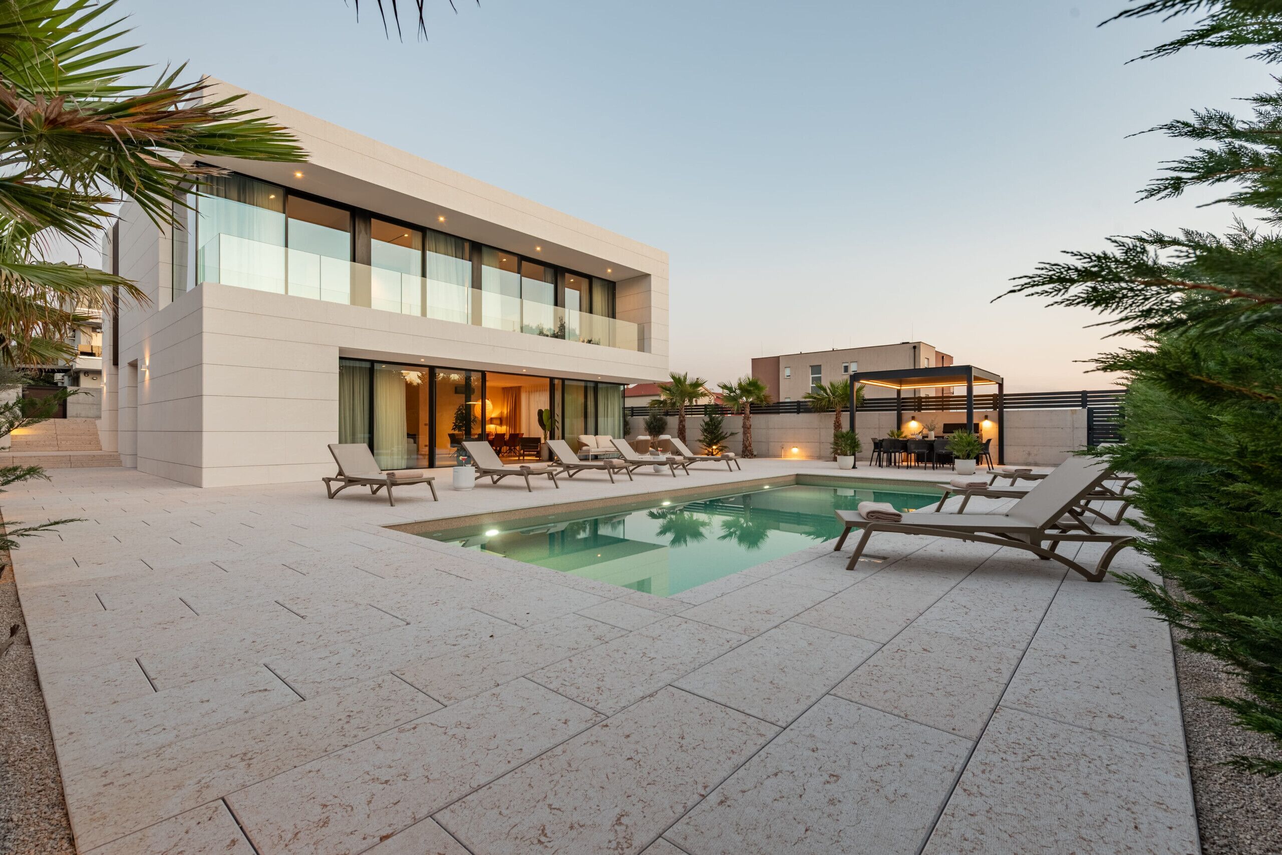 A modern two-story building with a swimming pool, lounge chairs, and outdoor seating.