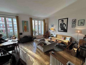 Un salon avec un canapé, une table, une chaise, un radiateur et une fenêtre avec des rideaux.