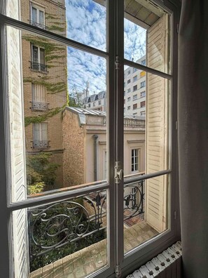 A window with a view of a narrow street, buildings with balconies, and a metal railing. - Very nice flat close to Panthéon (Paris)
