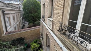 En bygning med flere etager, facade af mursten, en balkon med smedejernsgelænder og et træ i gården.
