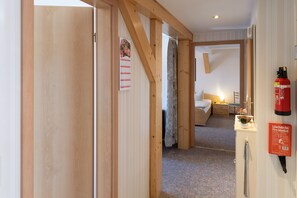 Habitación de hotel con puerta de madera, cama, mesita de noche, lámpara, extintor y un calendario en la pared.