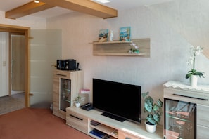 Ein modernes Wohnzimmer mit Flachbildfernseher, Holzbögen, einer Vitrine und einem Topf mit Pflanze.