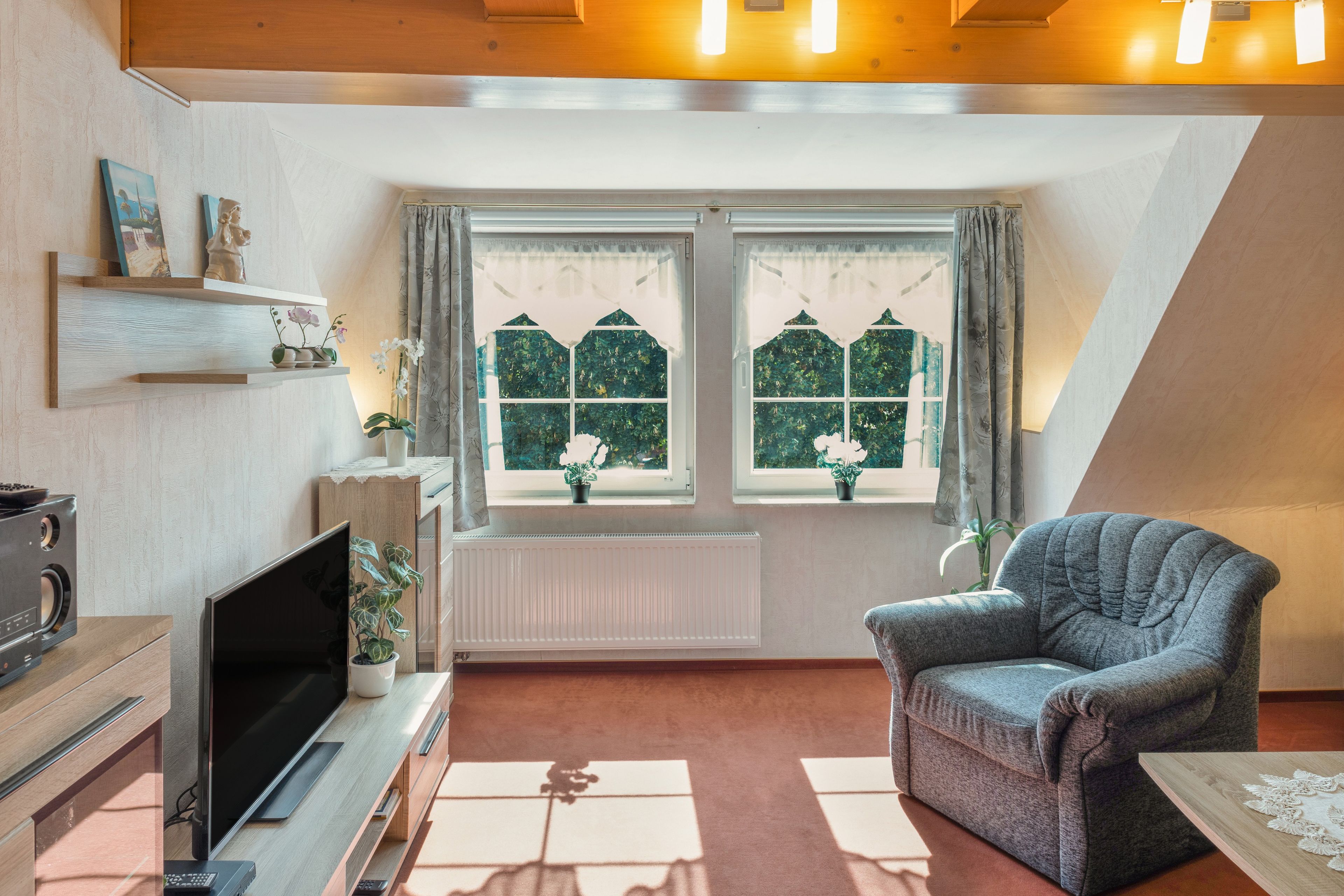 A living room with a television, a sofa, and a window with curtains.