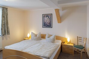 Un dormitorio con cama, dos mesitas de noche con lámparas, una silla, un cuadro en la pared y una ventana con cortinas.