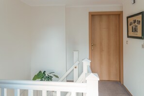 Una escalera con una puerta de madera en la parte superior, una barandilla blanca y un cuadro enmarcado en la pared.